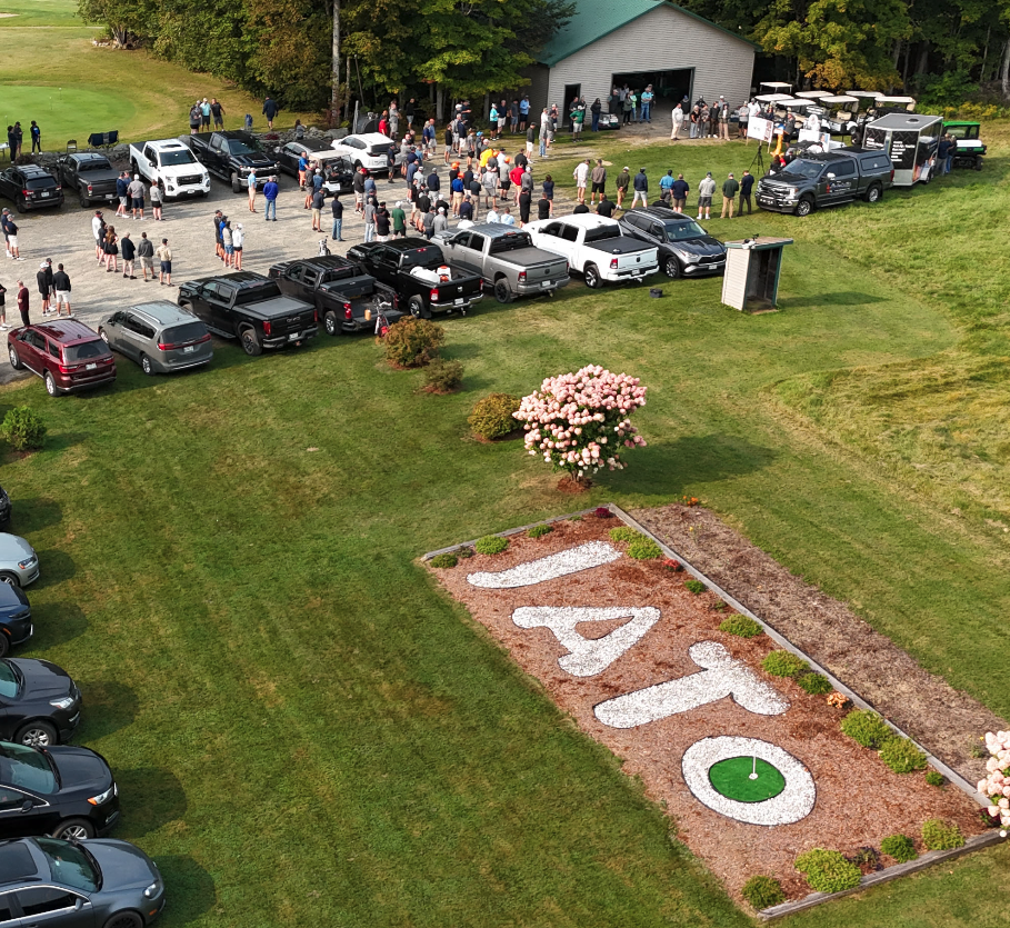 aerial photograph of a large group of people and vehicles at the 2024 professional logging contractors of the northeast's Log A Load golf tournament